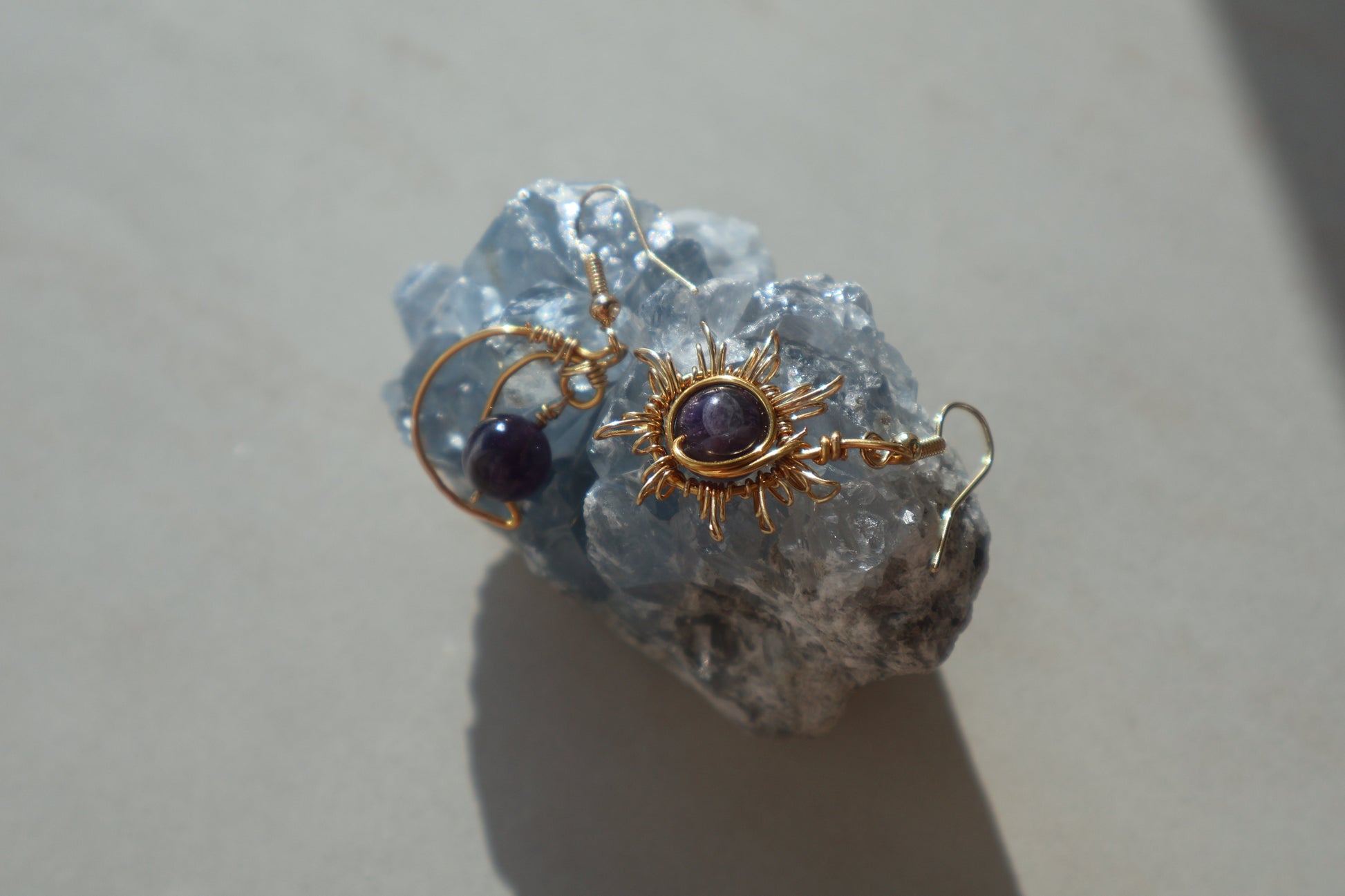Handmade Gemstone Sun and Moon Earrings with intricate wire-wrapped design placed on a crystal.