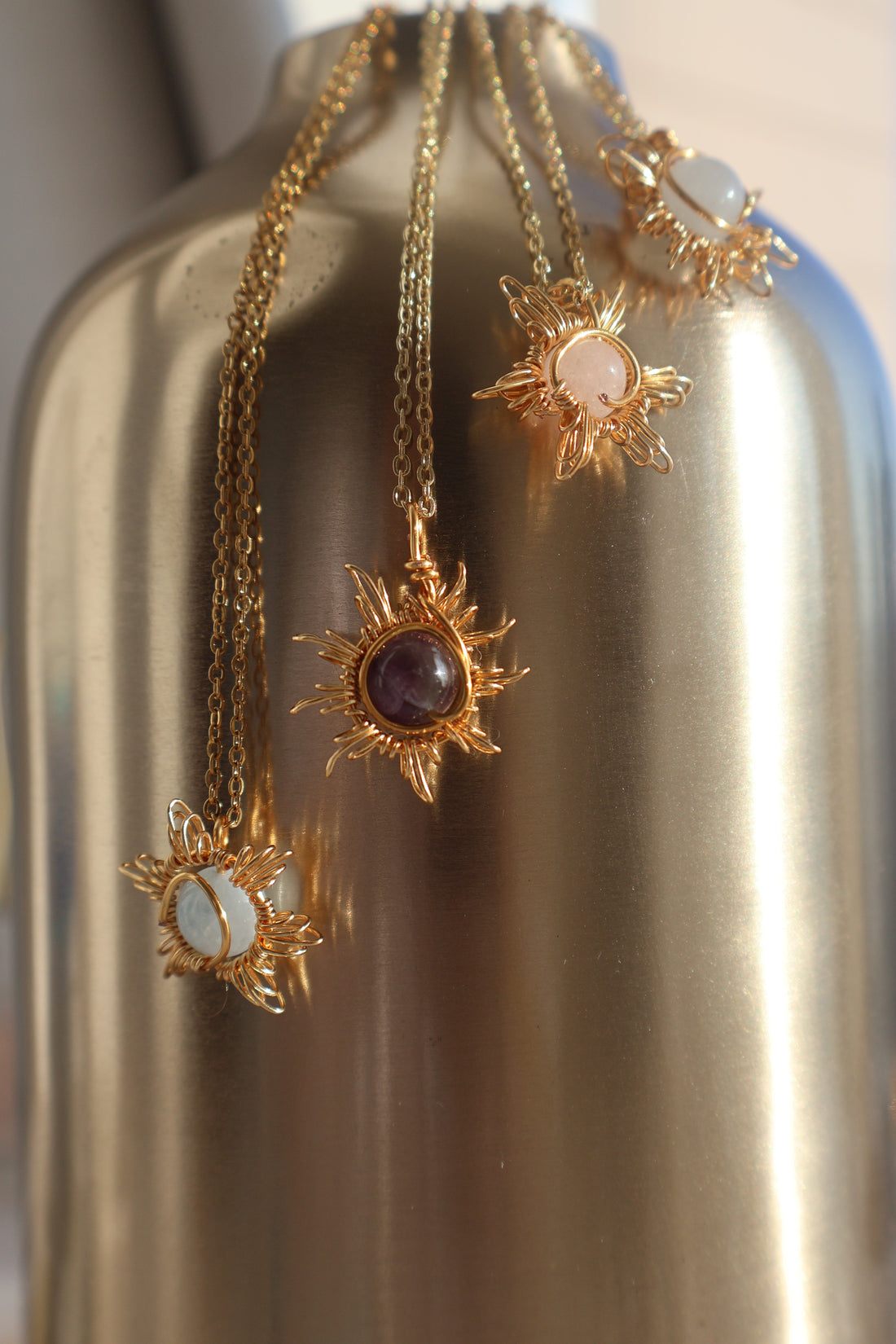 Sunburst Gemstone Necklace with intricate wire-wrapped sun design pendant on gold chains.