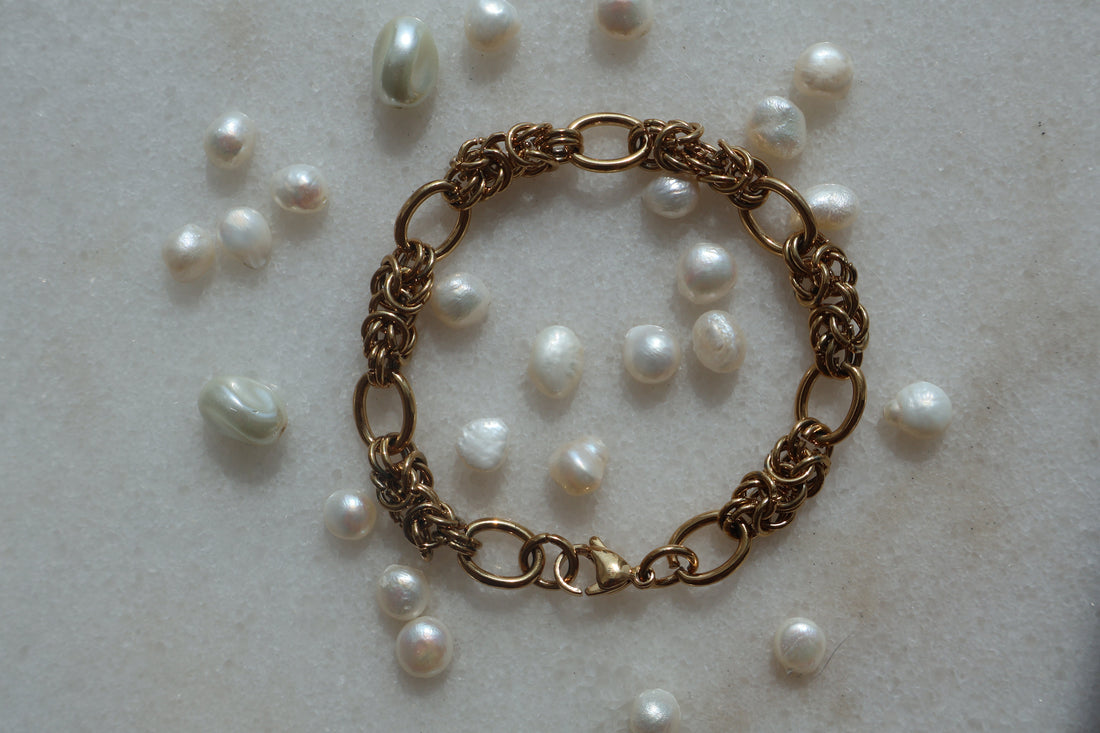 Vintage Gold Chain Bracelet with elegant design on marble surface surrounded by pearls.