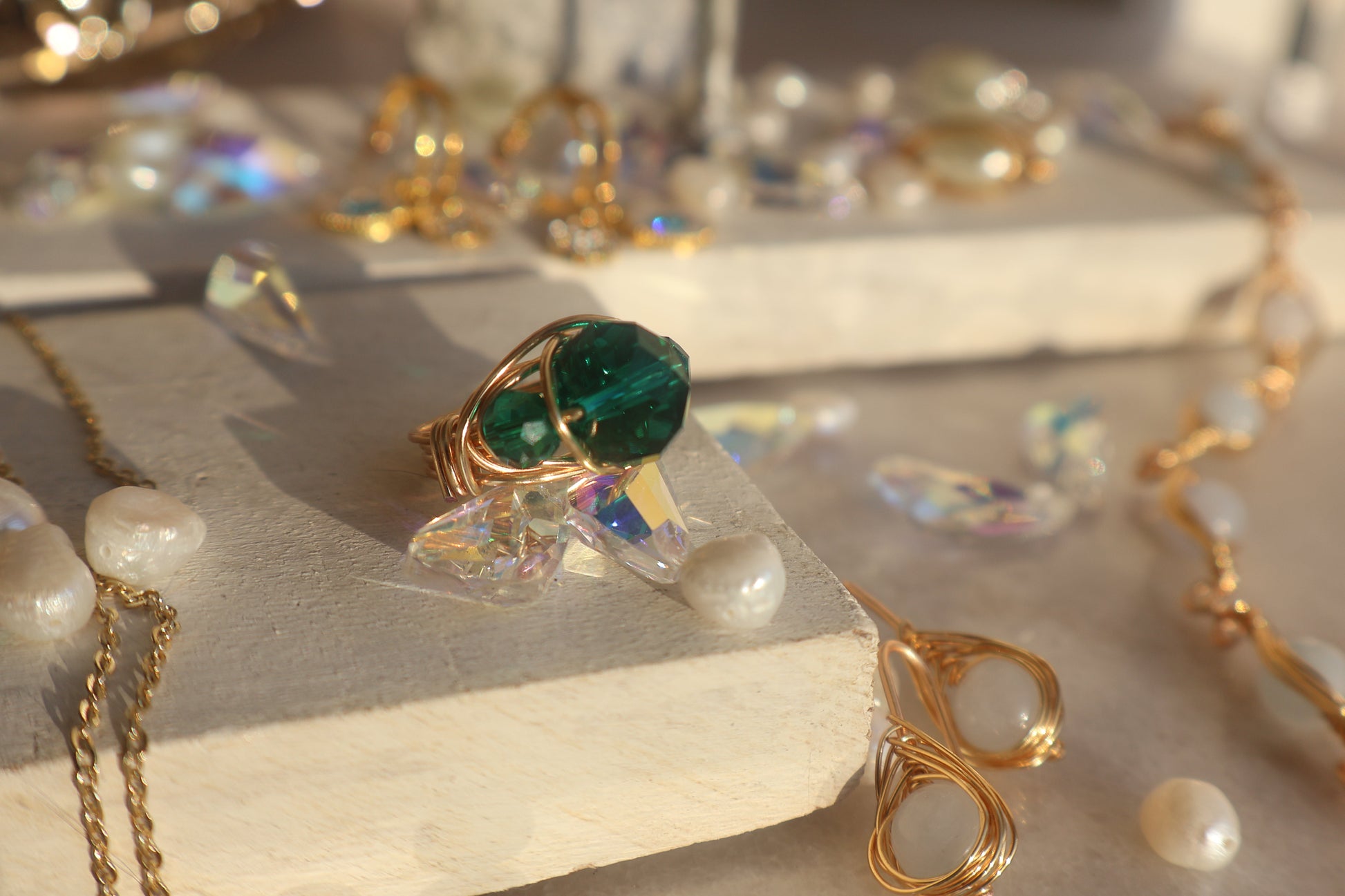 Gold emerald green bead ring with copper wire wrap on display amidst gemstones and jewelry.