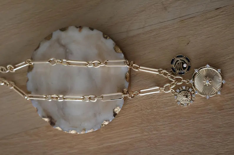 Gold paperclip round pendant necklace with charms on a decorative surface.