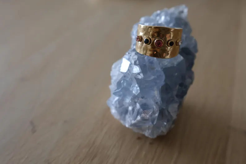 Elegant gold hammered ring with multicolored gemstones displayed on a crystal.