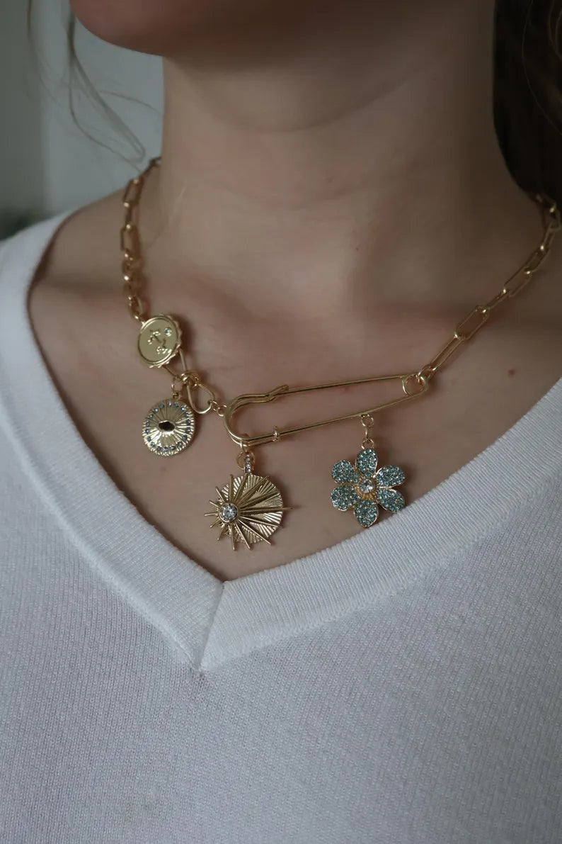 14k gold layered necklace with paperclip chain and safety pin pendant featuring charms.