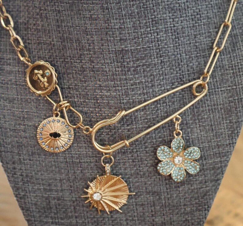 14k gold layered necklace with paperclip chain and safety pin pendant featuring charms.
