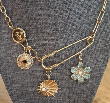14k gold layered necklace with paperclip chain and safety pin pendant featuring charms.